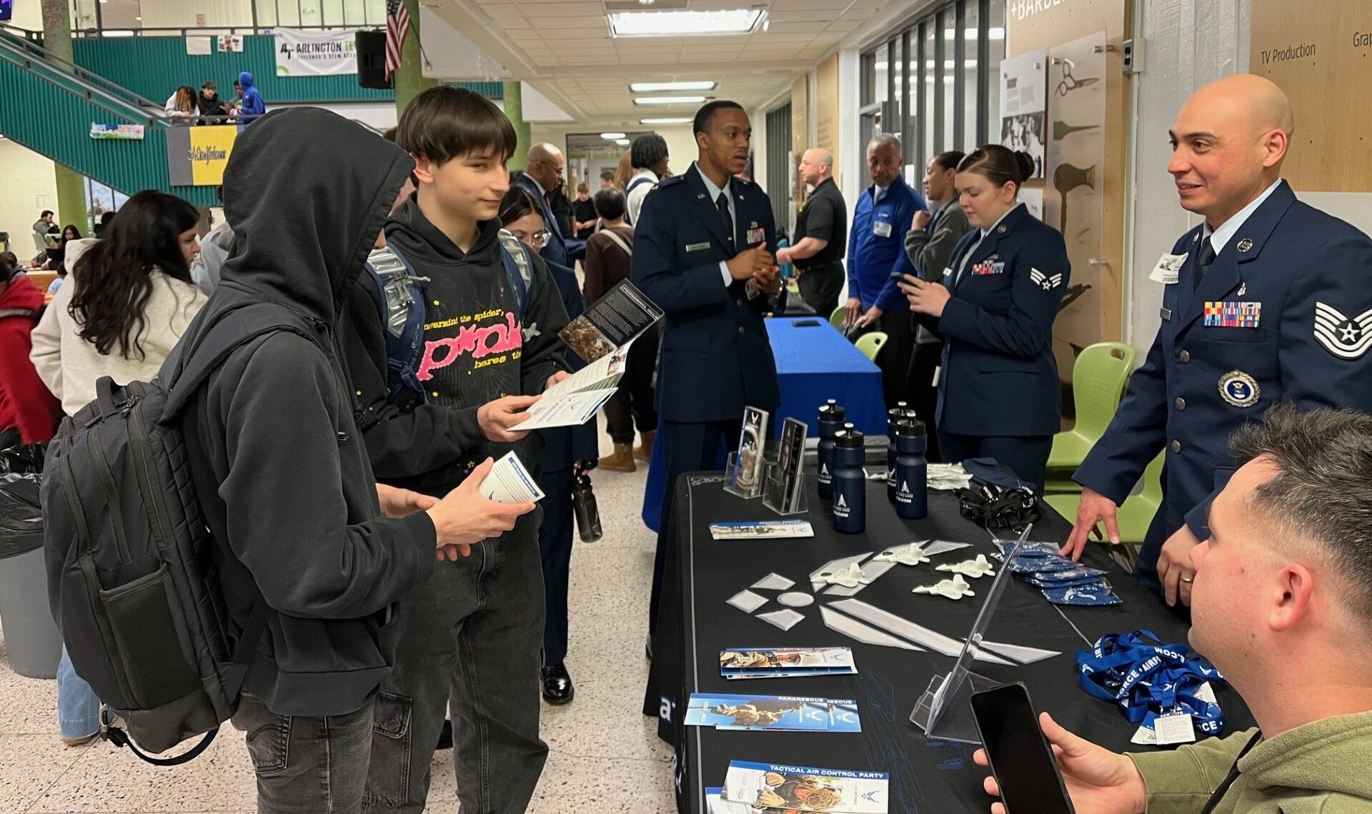 Air Force recruiters in uniform speak with students at a career expo booth, handing out brochures and discussing STEM and career opportunities.